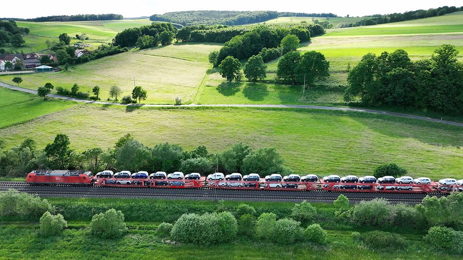 Car carrier wagons with new vehicles drive through green landscape