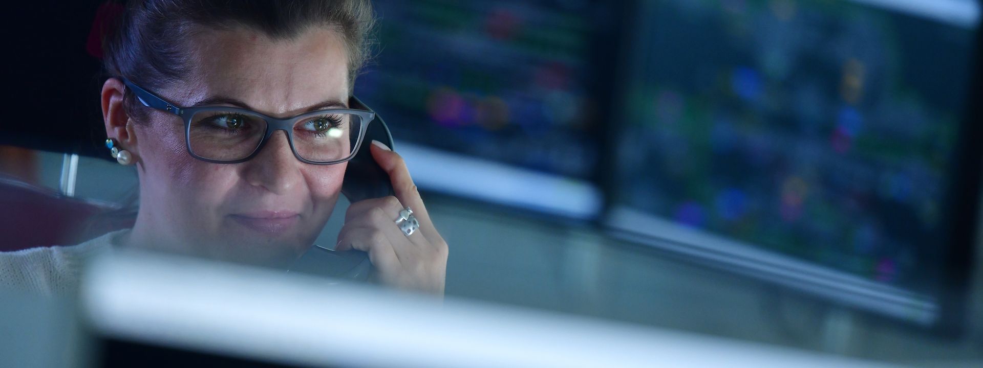 Frau mit Telefonhörer am Ohr in Zentrale mit vielen Computern