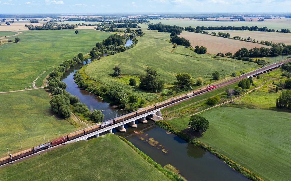 Landschaft mit einem Fluss. Zug fährt über eine Brücke