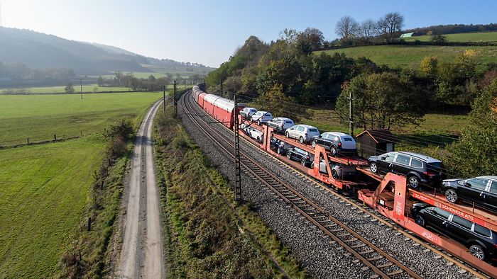 A train with car transporters travelling through a green landscape